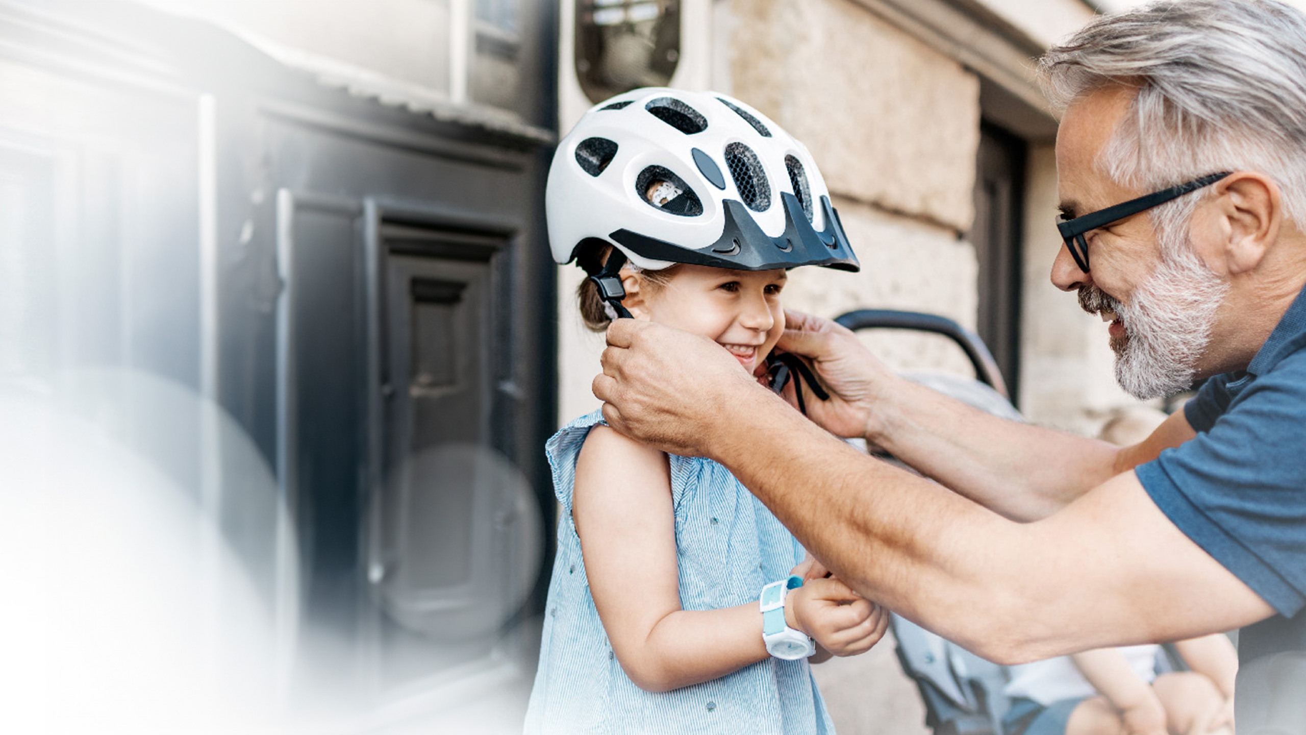 Mann setzt einem kleinen Mädchen einen Helm auf. Beide lächeln glücklich.