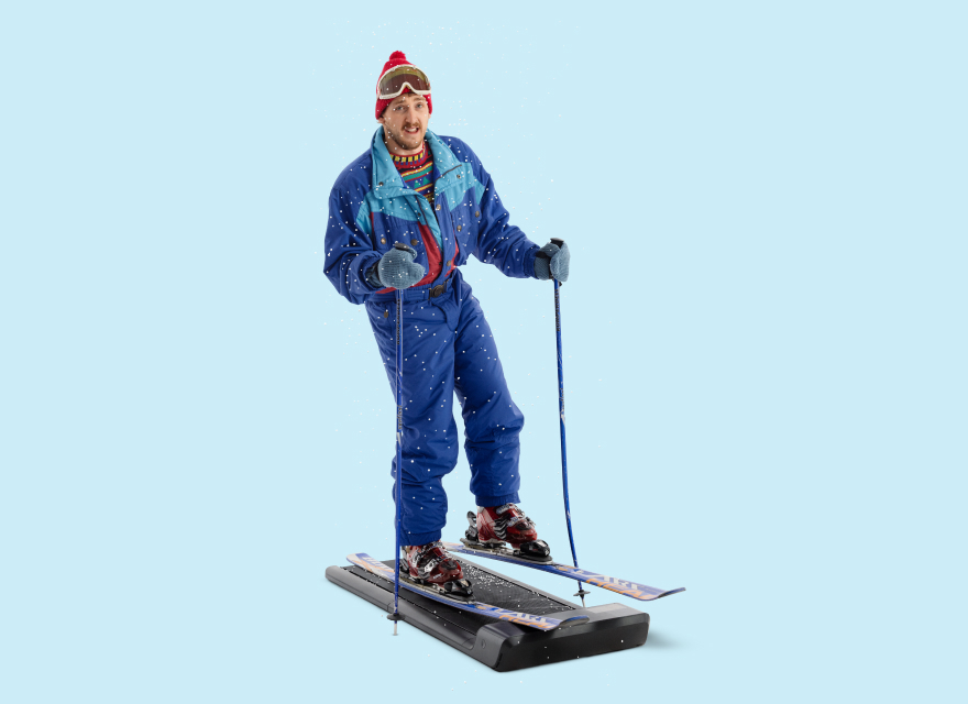 Paul mit Skikleidung und Pudelmütze auf Laufband mit Skiern und Skistöcken