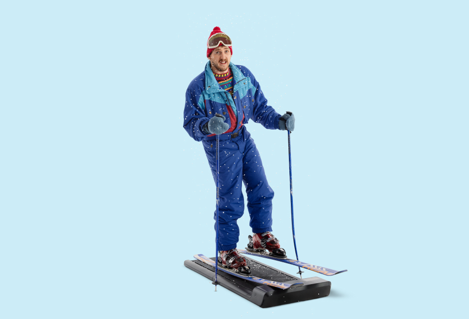 Paul mit Skikleidung und Pudelmütze auf Laufband mit Skiern und Skistöcken